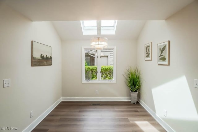 spare room with an inviting chandelier, hardwood / wood-style floors, and a skylight