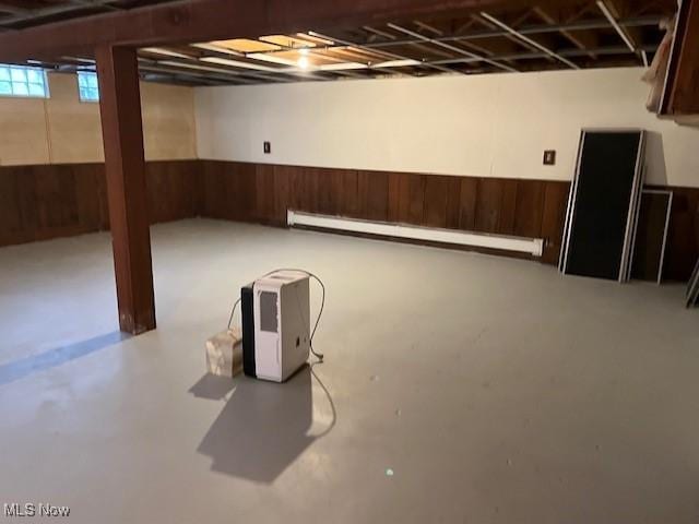 basement with a baseboard heating unit and wooden walls