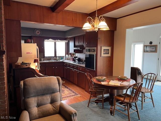 kitchen featuring sink, light hardwood / wood-style flooring, appliances with stainless steel finishes, beam ceiling, and a chandelier