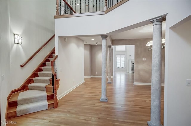 stairs with a towering ceiling, hardwood / wood-style floors, and ornate columns