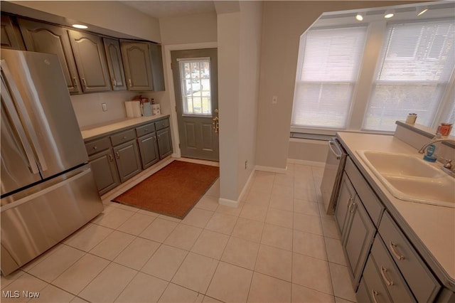 kitchen with gray cabinetry, sink, light tile patterned floors, and stainless steel appliances