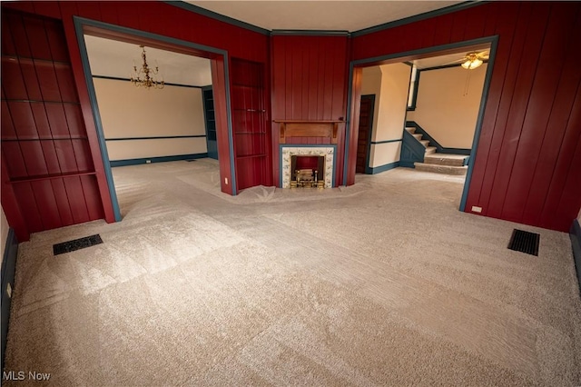 unfurnished living room featuring a tiled fireplace, a notable chandelier, wooden walls, and light colored carpet