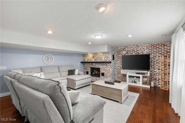 living room featuring a brick fireplace, dark hardwood / wood-style floors, a textured ceiling, and brick wall