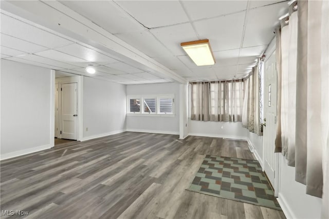 basement featuring a drop ceiling, baseboards, and wood finished floors