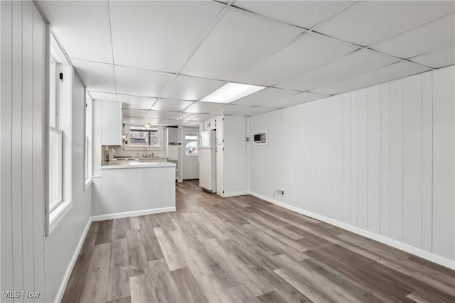 unfurnished living room featuring light wood-style floors, baseboards, and a drop ceiling