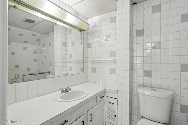 bathroom featuring toilet, visible vents, vanity, tile walls, and tasteful backsplash