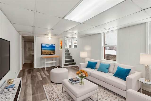 living room with a paneled ceiling, wood finished floors, baseboards, and stairs