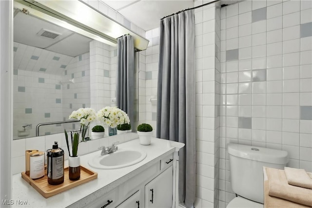 full bathroom with toilet, visible vents, vanity, and tile walls