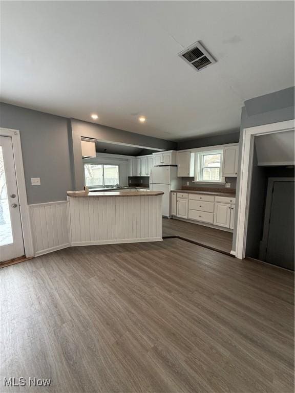 kitchen featuring a peninsula, visible vents, wainscoting, freestanding refrigerator, and dark wood finished floors