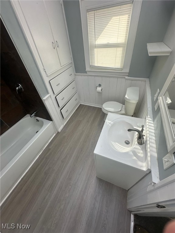 bathroom with toilet, a wainscoted wall, wood finished floors, a bathtub, and vanity