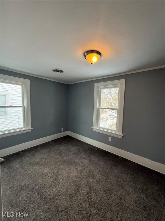 unfurnished room featuring crown molding, dark carpet, visible vents, and baseboards