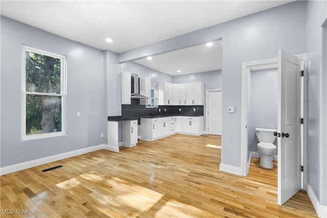 kitchen featuring white cabinetry, wall chimney exhaust hood, decorative backsplash, and light hardwood / wood-style flooring