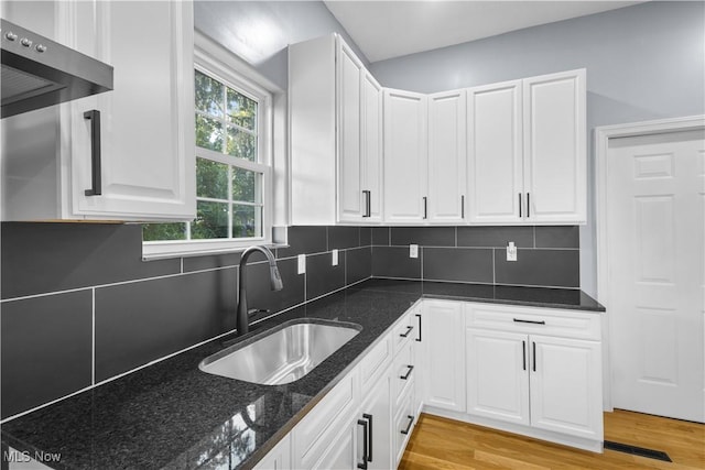 kitchen with white cabinetry, sink, backsplash, and dark stone counters