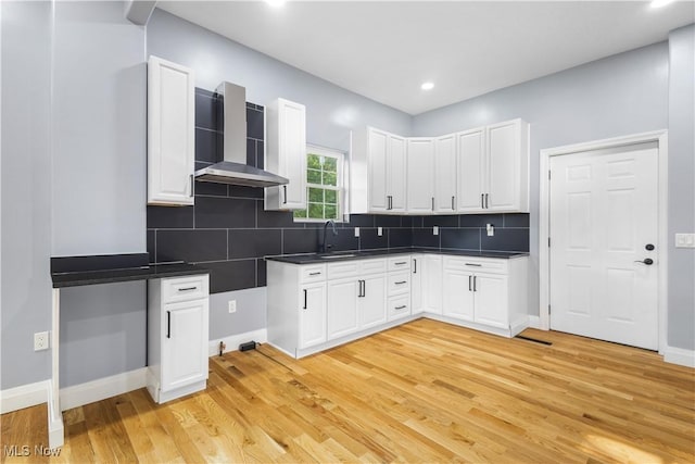 kitchen featuring white cabinets, light hardwood / wood-style floors, sink, and wall chimney range hood