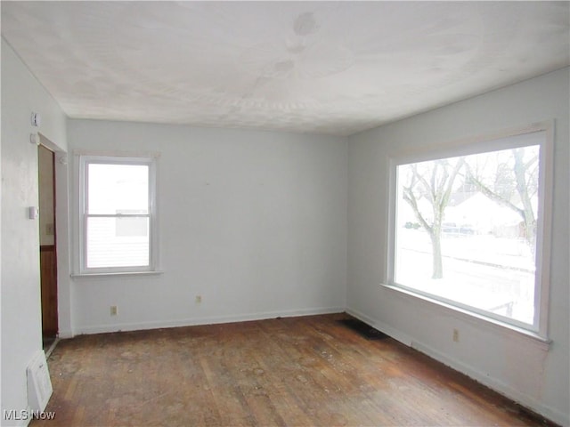 empty room featuring plenty of natural light, baseboards, and dark wood-type flooring