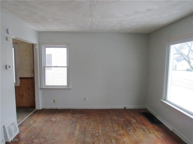 spare room featuring dark wood-style floors, visible vents, and plenty of natural light