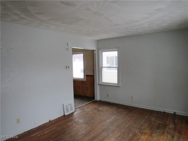 spare room with dark wood-style flooring, visible vents, and baseboards