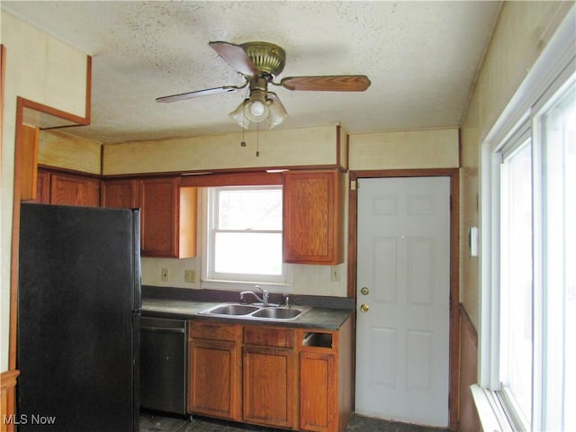 kitchen featuring a textured ceiling, a sink, brown cabinets, black appliances, and dark countertops