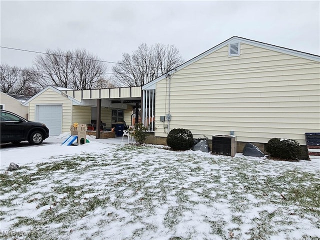 snow covered property with a garage and central AC unit