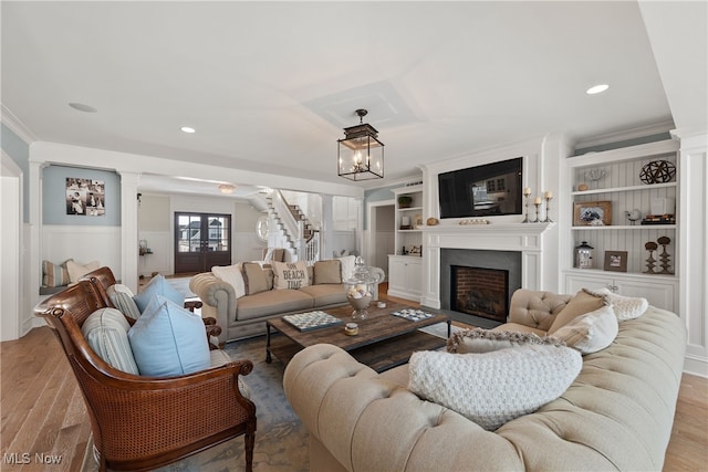 living room with built in shelves, a large fireplace, ornamental molding, and light wood-type flooring