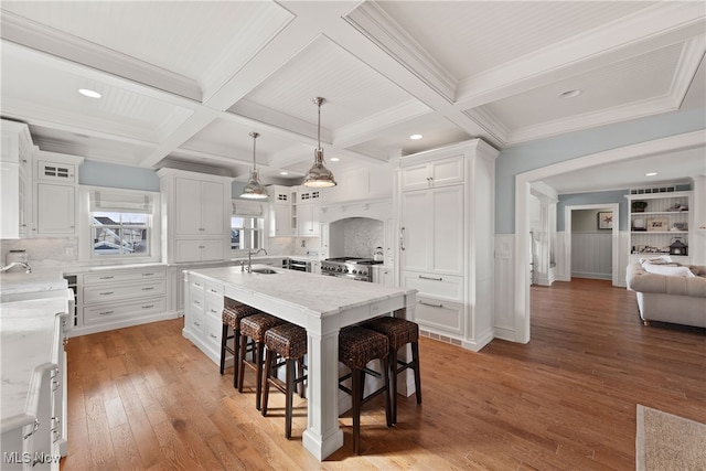 kitchen with high end range, hanging light fixtures, a kitchen breakfast bar, an island with sink, and white cabinets