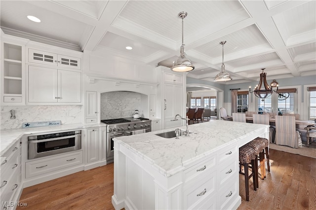 kitchen with sink, hanging light fixtures, a center island with sink, double oven range, and white cabinets