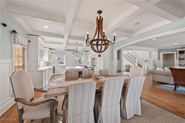 dining area with decorative columns, coffered ceiling, crown molding, beam ceiling, and light hardwood / wood-style flooring