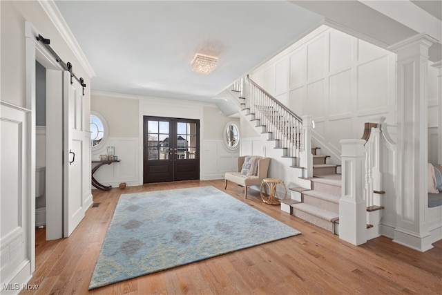 foyer entrance featuring crown molding, a barn door, light hardwood / wood-style floors, and french doors