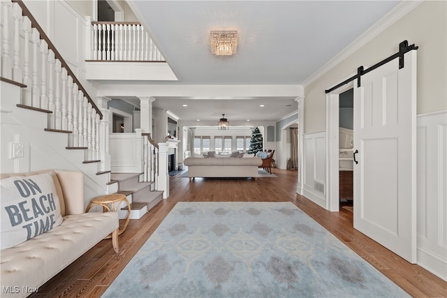 foyer entrance featuring crown molding, hardwood / wood-style floors, ceiling fan, a barn door, and decorative columns