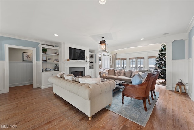 living room featuring hardwood / wood-style floors, built in shelves, ornamental molding, and decorative columns