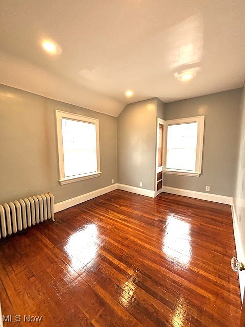 unfurnished room featuring dark hardwood / wood-style flooring, radiator heating unit, lofted ceiling, and a healthy amount of sunlight