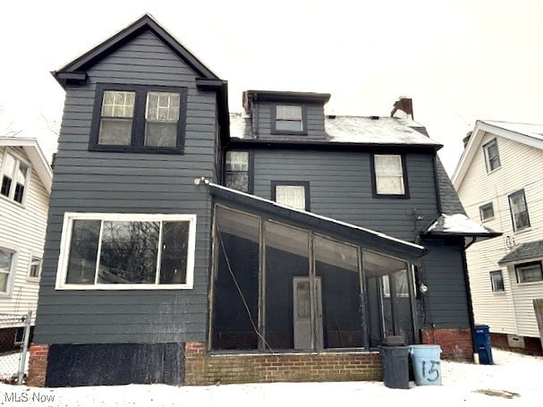 snow covered back of property featuring a sunroom