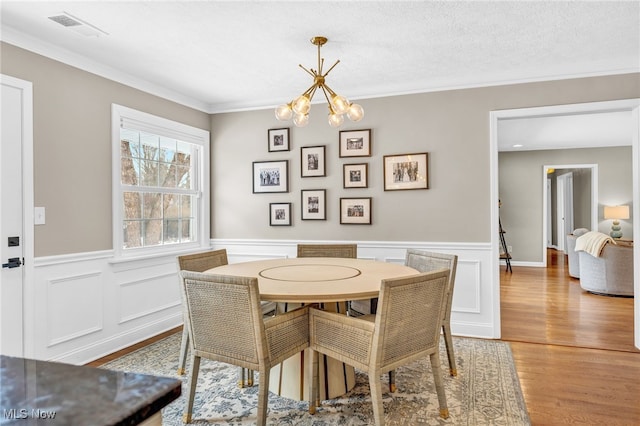 dining area featuring wood-type flooring, a textured ceiling, a notable chandelier, and crown molding