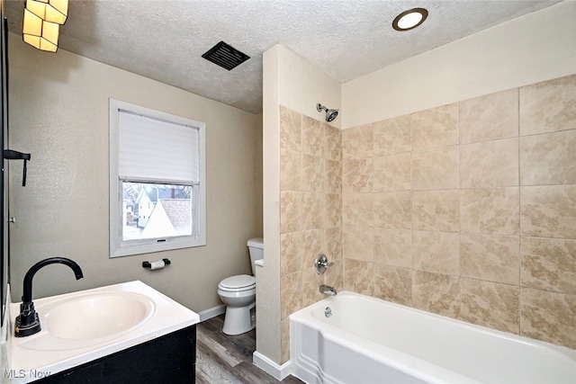 full bathroom featuring hardwood / wood-style flooring, tiled shower / bath combo, vanity, a textured ceiling, and toilet