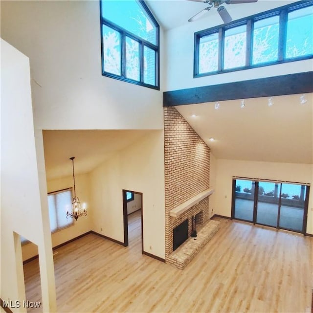 unfurnished living room featuring ceiling fan with notable chandelier, a fireplace, high vaulted ceiling, and light hardwood / wood-style flooring