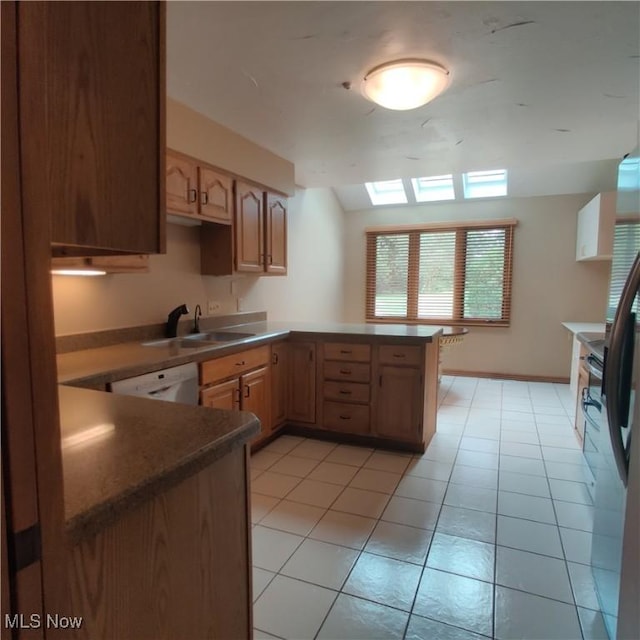 kitchen with light tile patterned flooring, lofted ceiling with skylight, sink, white dishwasher, and kitchen peninsula