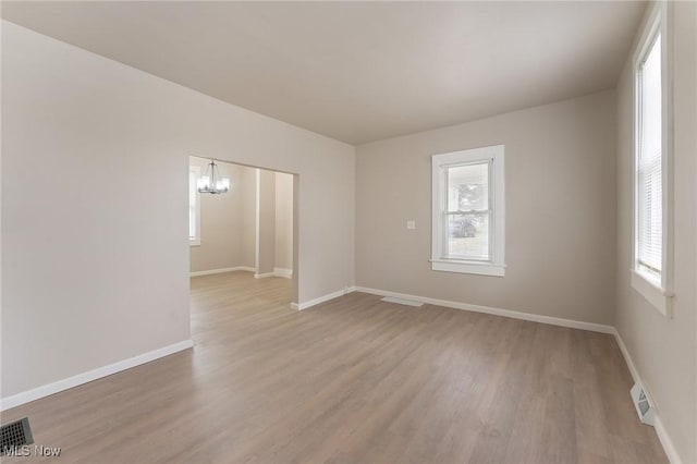 spare room with an inviting chandelier, a wealth of natural light, and light wood-type flooring