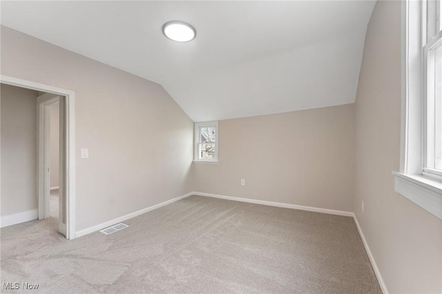 additional living space featuring light colored carpet and vaulted ceiling