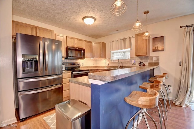 kitchen with a breakfast bar area, hanging light fixtures, light brown cabinets, kitchen peninsula, and stainless steel appliances