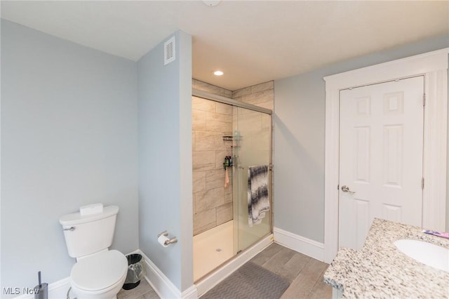 bathroom with hardwood / wood-style flooring, vanity, a shower with shower door, and toilet