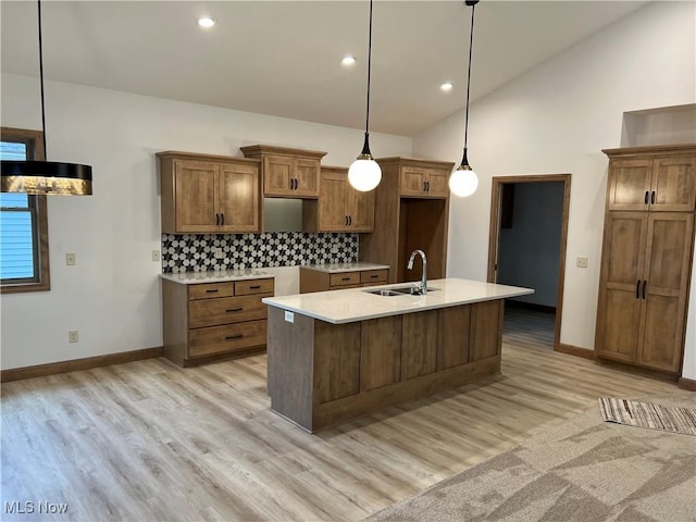 kitchen featuring lofted ceiling, sink, hanging light fixtures, a center island with sink, and backsplash