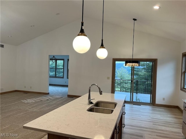 kitchen featuring high vaulted ceiling, decorative light fixtures, sink, light stone counters, and a center island with sink