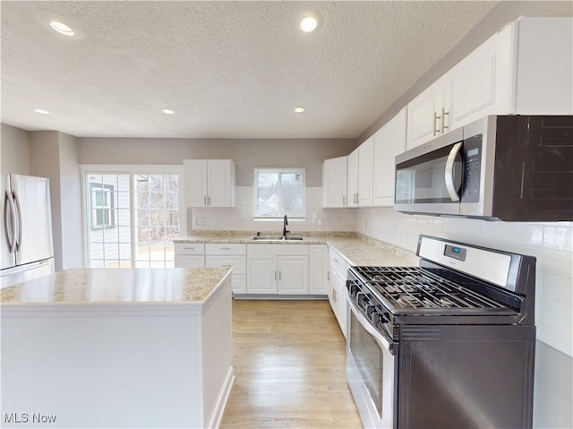 kitchen with sink, appliances with stainless steel finishes, white cabinetry, a kitchen island, and light wood-type flooring