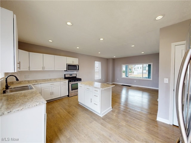 kitchen with sink, stainless steel appliances, white cabinets, a kitchen island, and light wood-type flooring