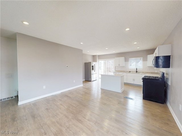 kitchen with a kitchen island, white cabinetry, sink, stove, and stainless steel fridge with ice dispenser