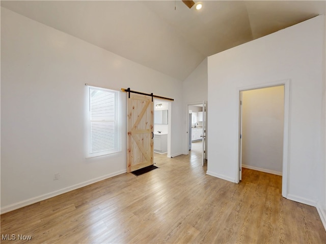 unfurnished bedroom with high vaulted ceiling, a spacious closet, light hardwood / wood-style floors, and a barn door