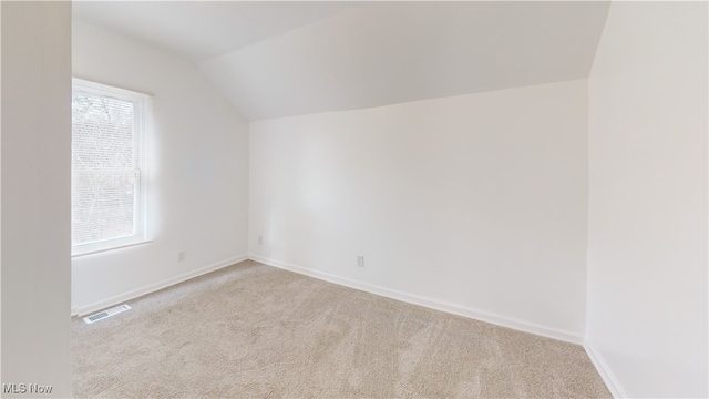 unfurnished room with vaulted ceiling, light colored carpet, and plenty of natural light