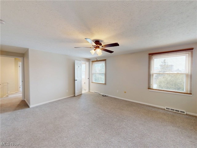 empty room with ceiling fan, light carpet, and a textured ceiling