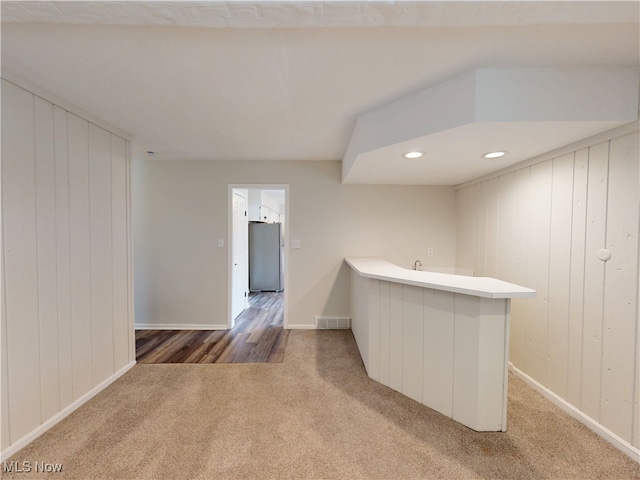 interior space with white cabinetry, dark carpet, stainless steel refrigerator, and wood walls