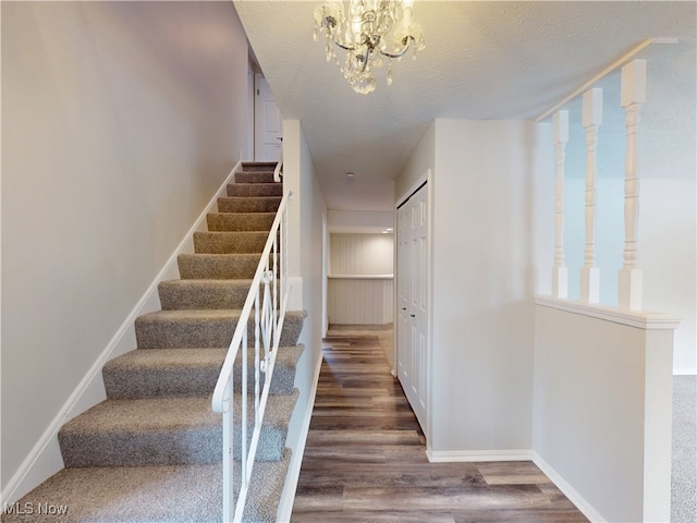 stairs with an inviting chandelier, wood-type flooring, and a textured ceiling